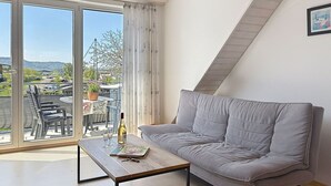 Ett modernt rum med en grå soffa, ett träbord och utsikt över en balkong med utemöbler och ett bord.