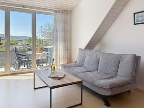 Une pièce moderne avec un canapé gris, une table basse en bois et une vue sur un balcon aménagé avec des sièges et une table.