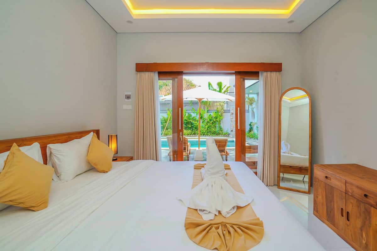 A hotel room with a bed, a wooden headboard, a mirror, and a view of an outdoor pool area.