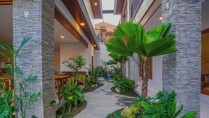 Un couloir avec un mur en pierre, des plantes d’intérieur, un banc et, au loin, une vue sur un bâtiment traditionnel.