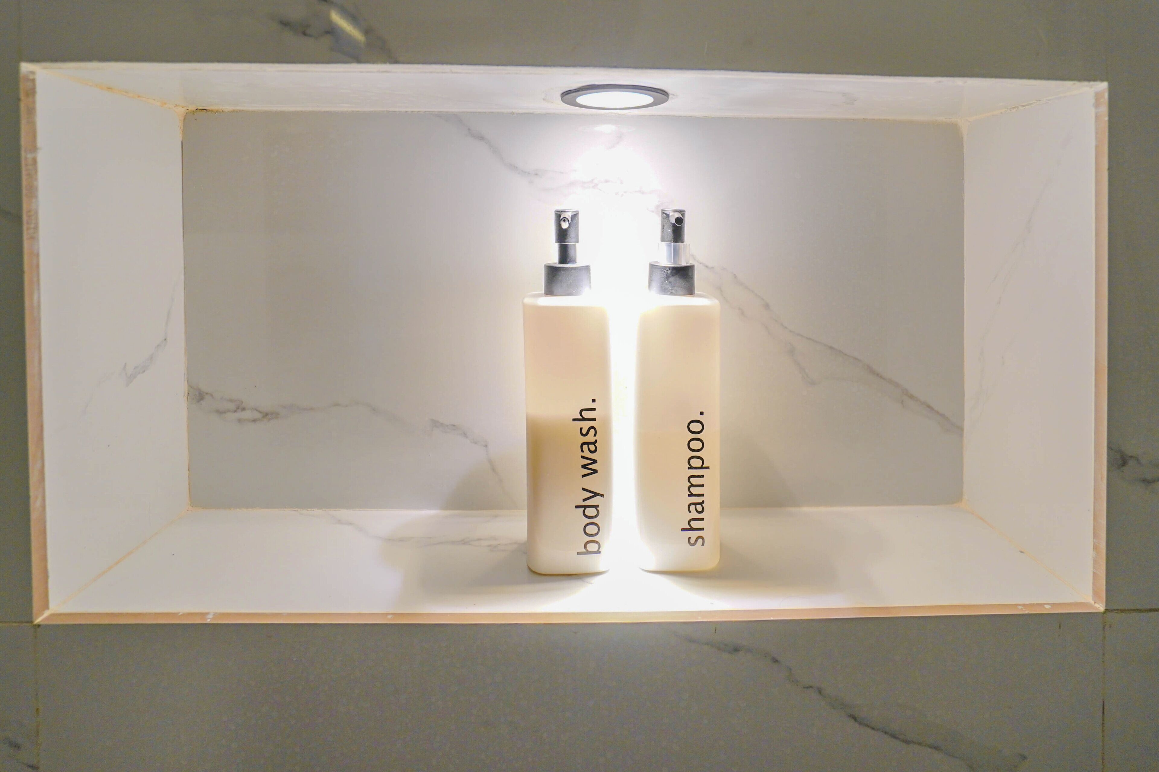Une salle de bain avec un lavabo en marbre et deux bouteilles étiquetées « gel douche » et « shampoing » posées sur une étagère.