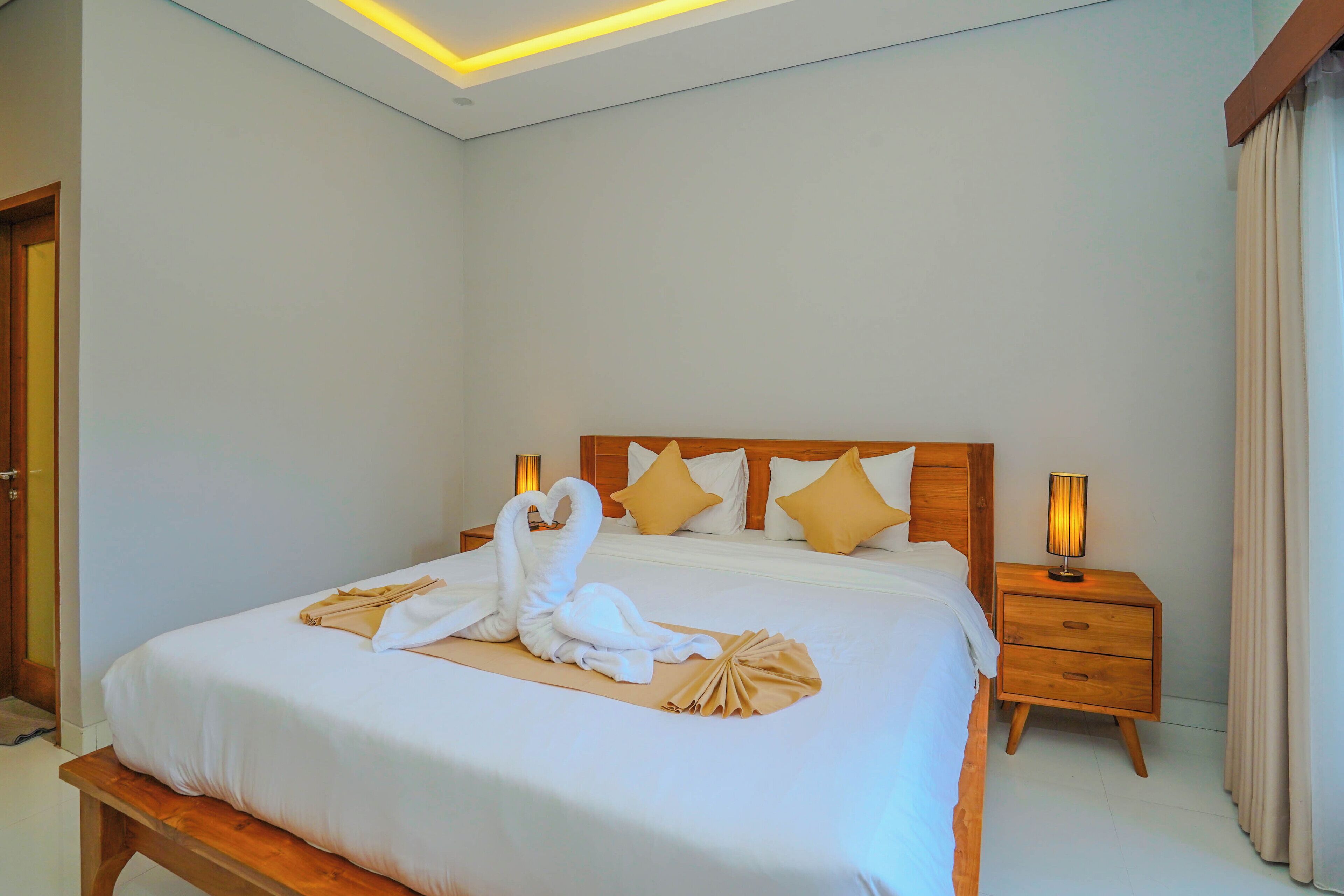 A hotel room with a neatly made bed, a wooden headboard, two bedside tables with lamps, and a wooden bench at the foot of the bed.