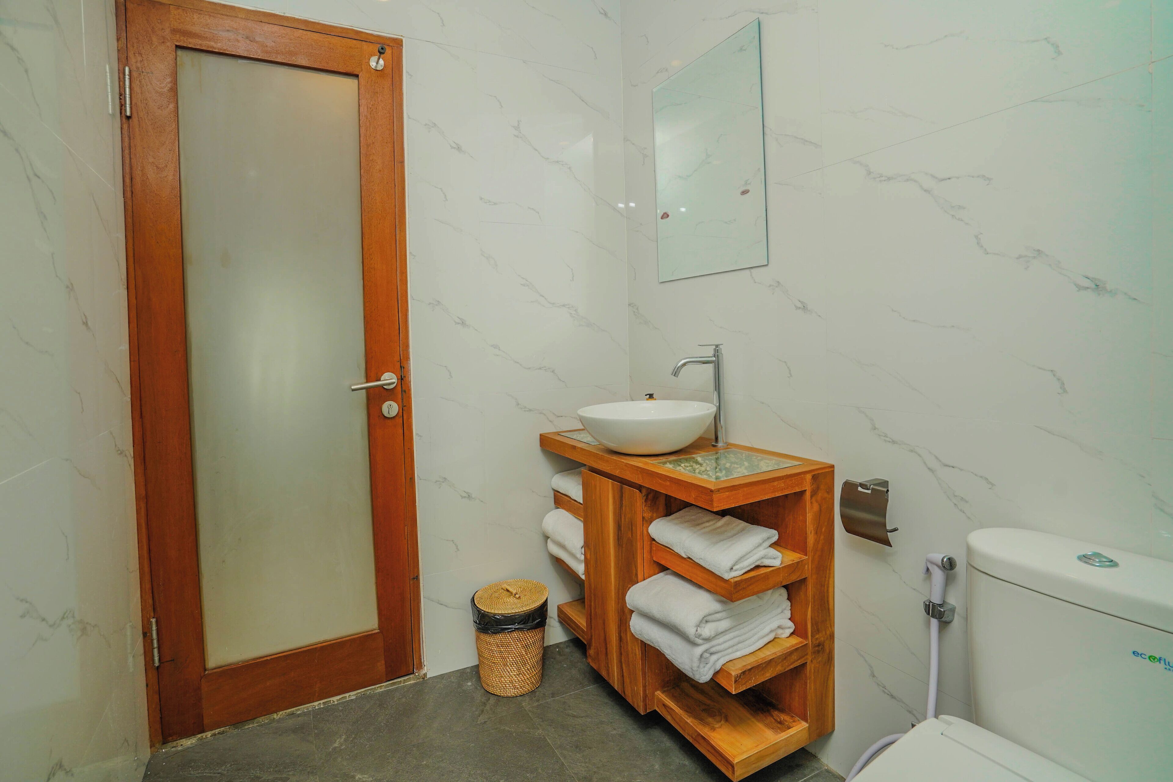 A bathroom with a wooden door, a white sink with a marble countertop, a mirror, and a toilet.