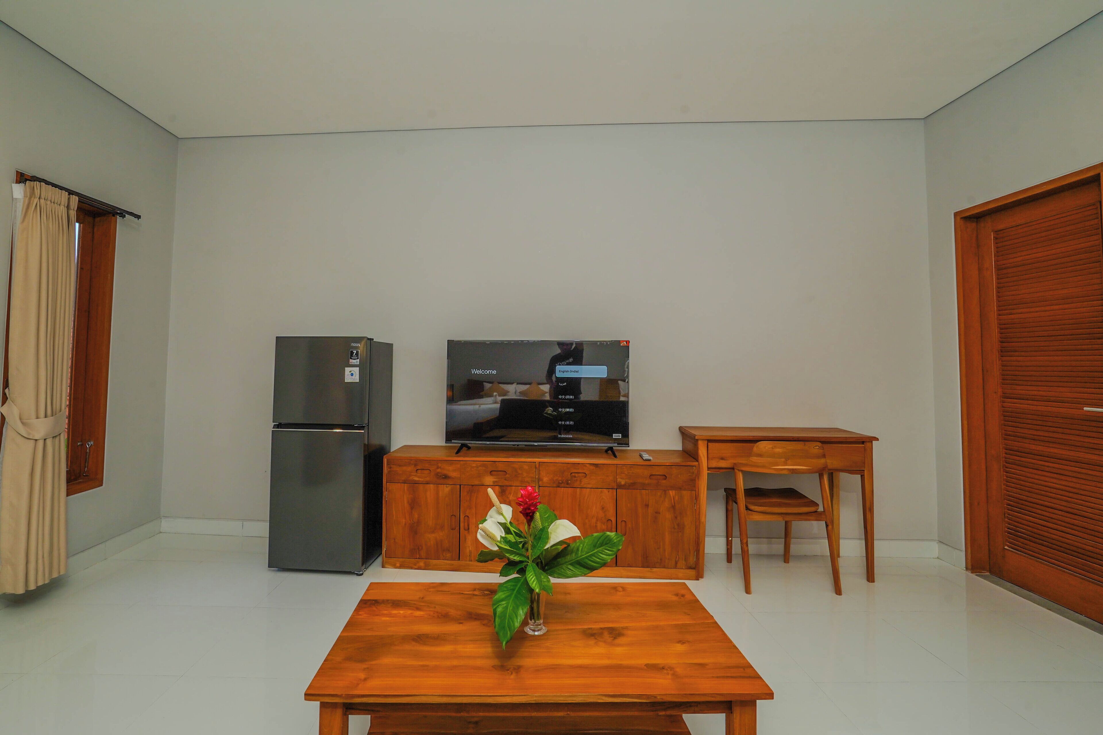 A small, clean room with a wooden table, a TV, a refrigerator, and a wooden cabinet.