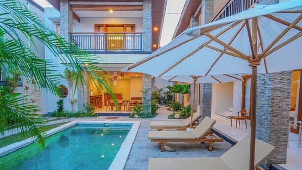 Un espace aménagé au bord de la piscine, avec des chaises longues et des parasols, un coin repas et un escalier menant à un niveau supérieur.