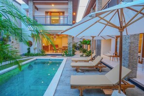 Ein Poolbereich mit Liegestühlen und Sonnenschirmen, ein Essbereich und eine Treppe, die zu einer oberen Ebene führt.