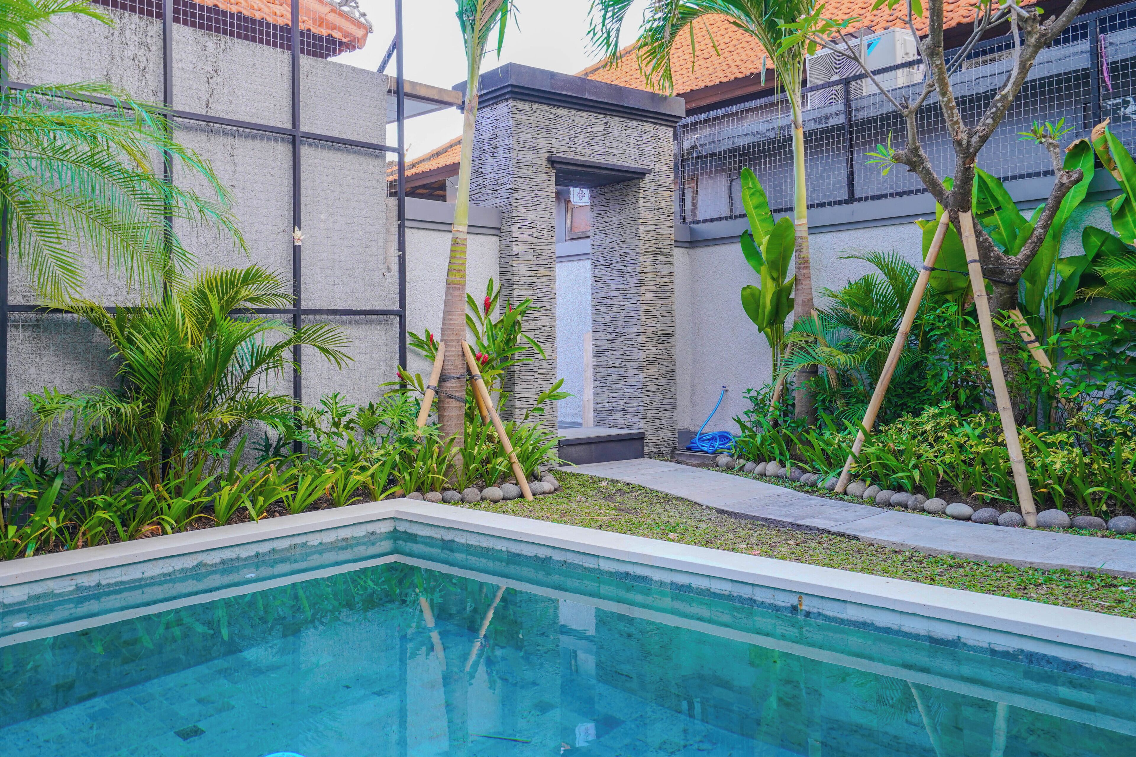 Una piscina rodeada de abundante vegetación y un muro de piedra.