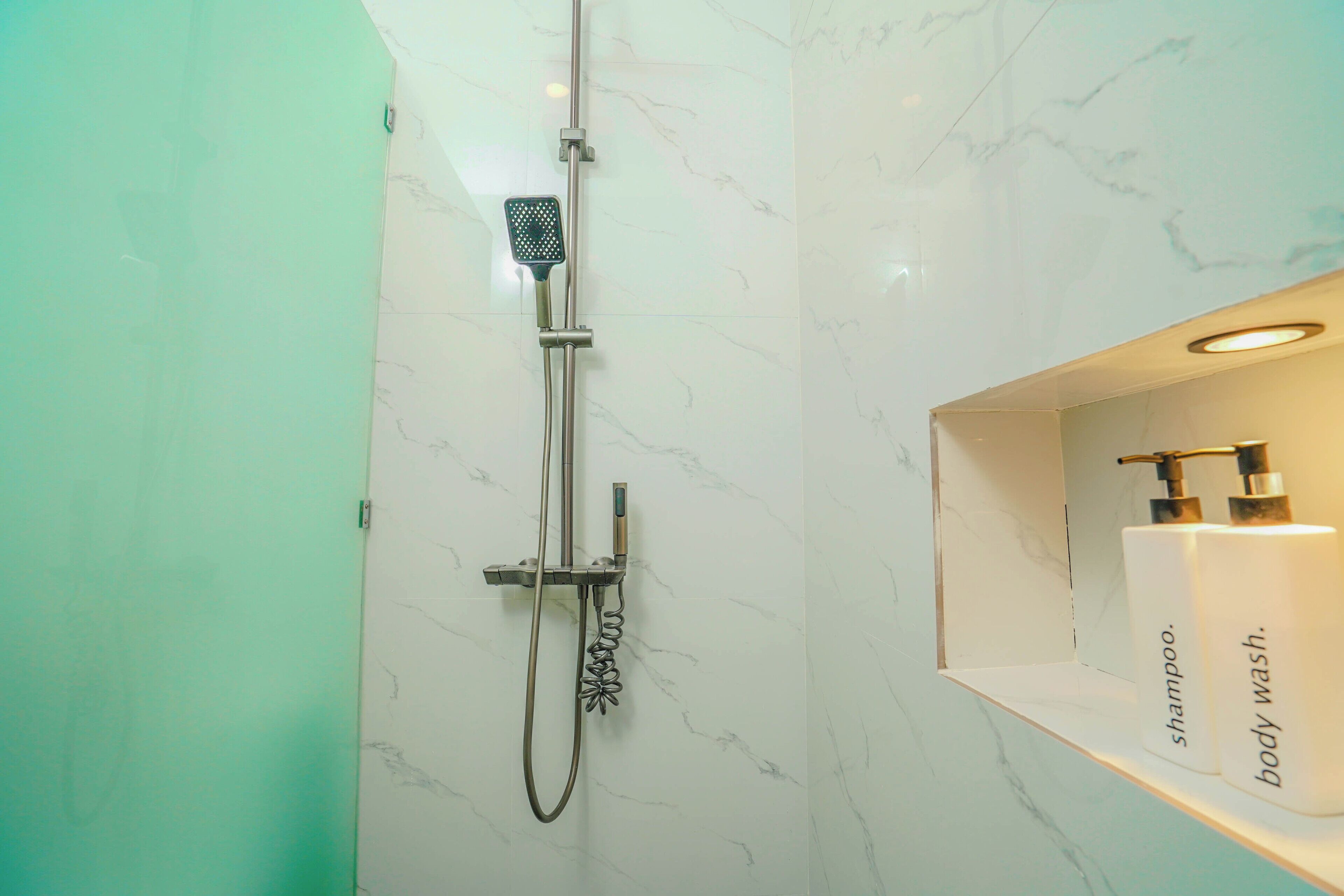 A bathroom with a shower, a marble wall, and a shelf with shampoo and body wash bottles.