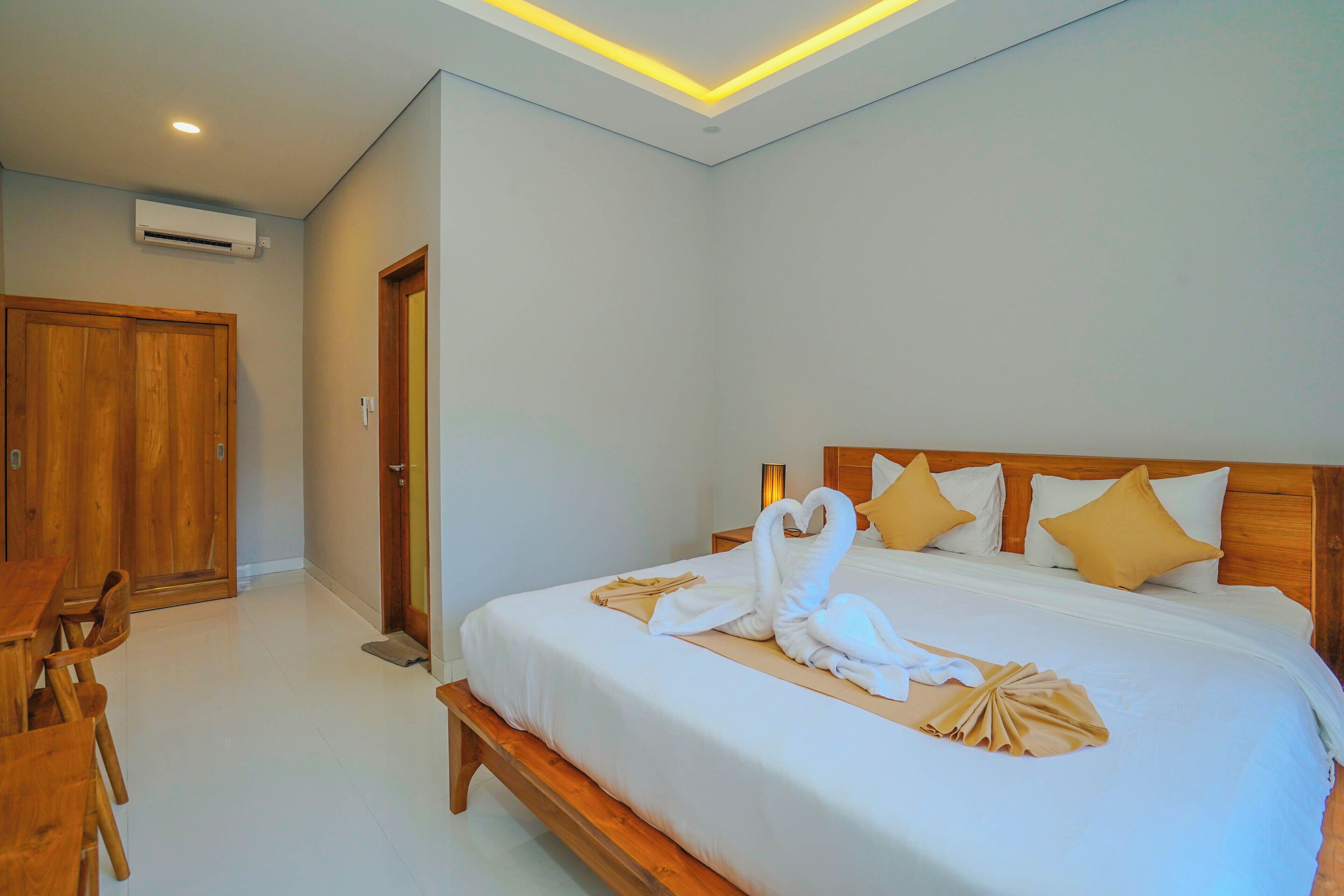 Habitación de hotel con una cama bien tendida, un banco de madera, un escritorio y una silla.