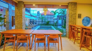 Un espace repas avec vue sur la piscine, doté de meubles en bois et de piliers en pierre.
