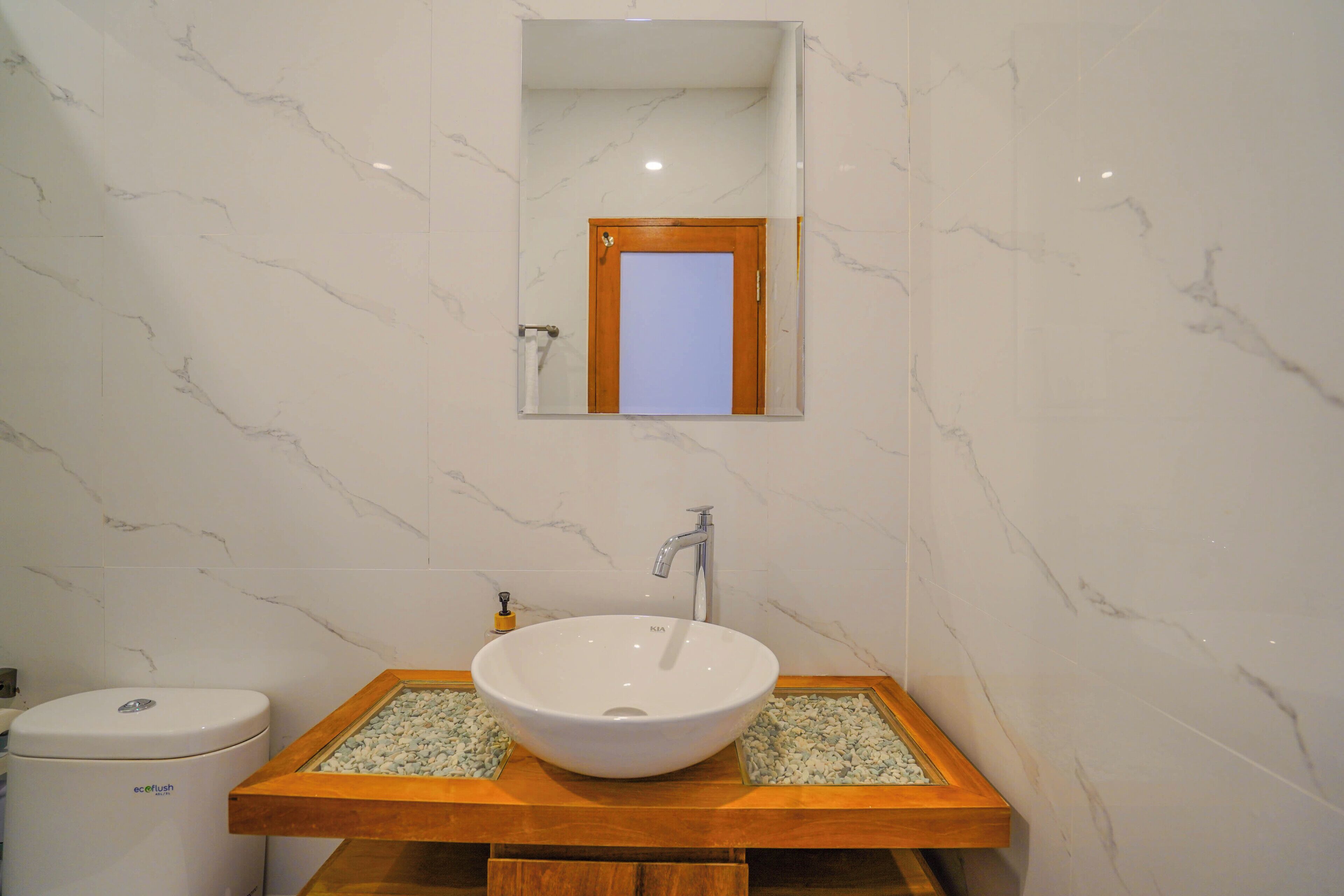 A bathroom with a white sink, wooden vanity, marble walls, and a mirror above the sink.