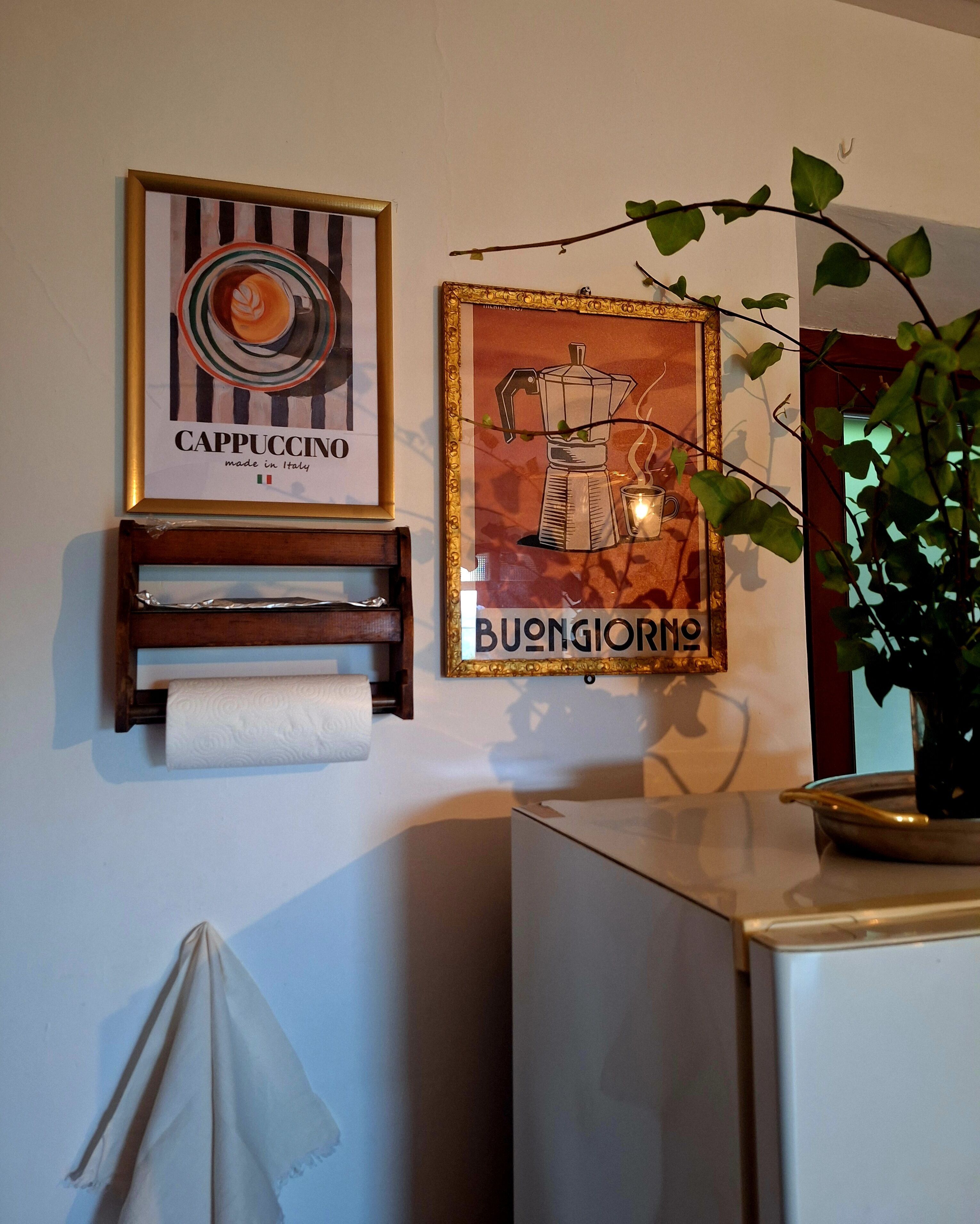 A wall with two framed pictures, a paper towel dispenser, and a potted plant.