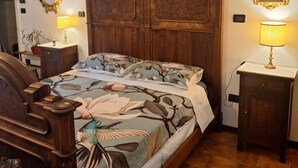 A bedroom with a wooden bed, two bedside tables, a nightstand, a mirror, and a wall-mounted picture.