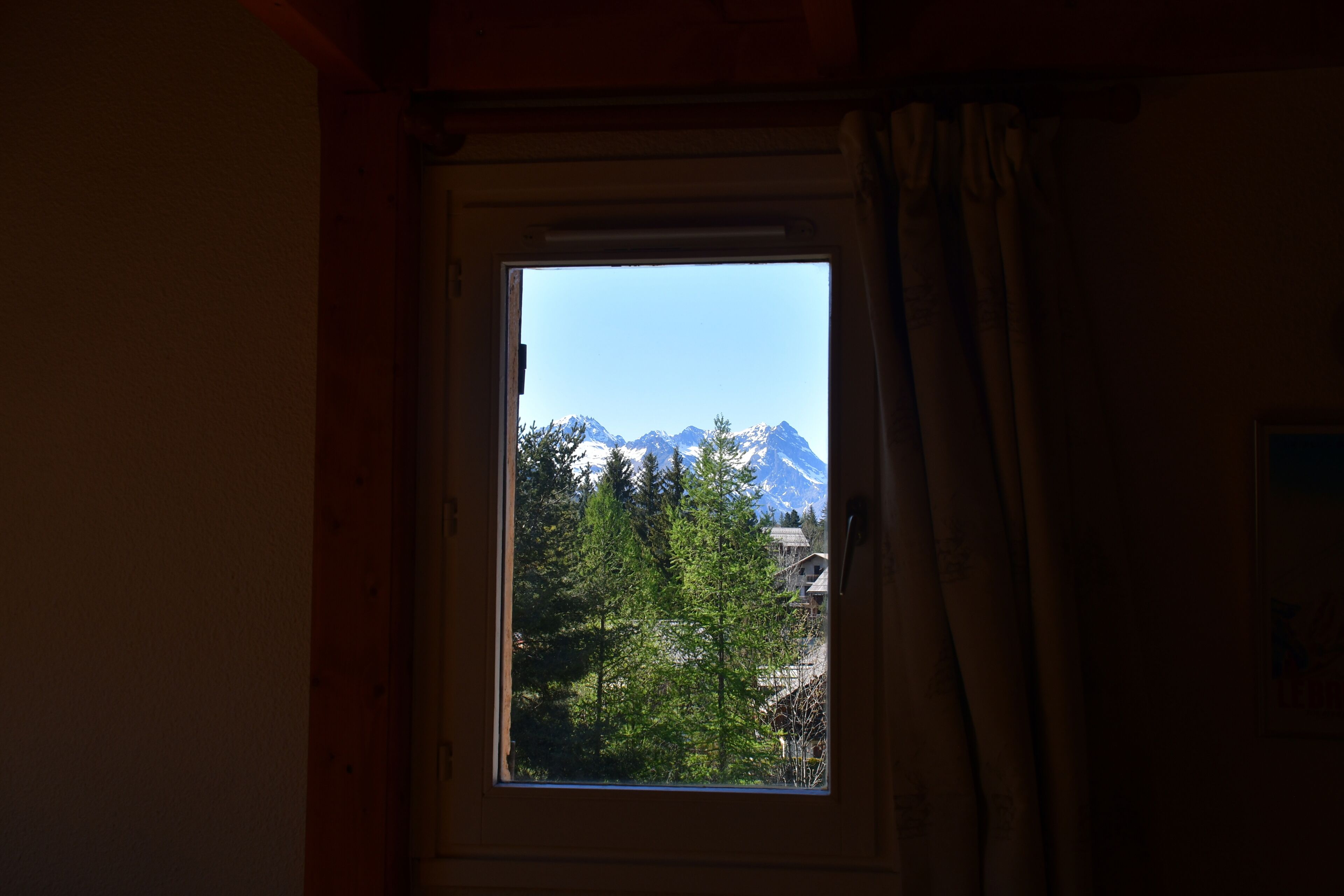 A window with a view of snow-capped mountains and trees.