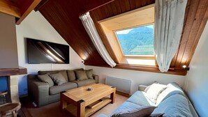 Une pièce chaleureuse avec un plafond en bois, un canapé, une table basse, un téléviseur et une fenêtre avec des rideaux.