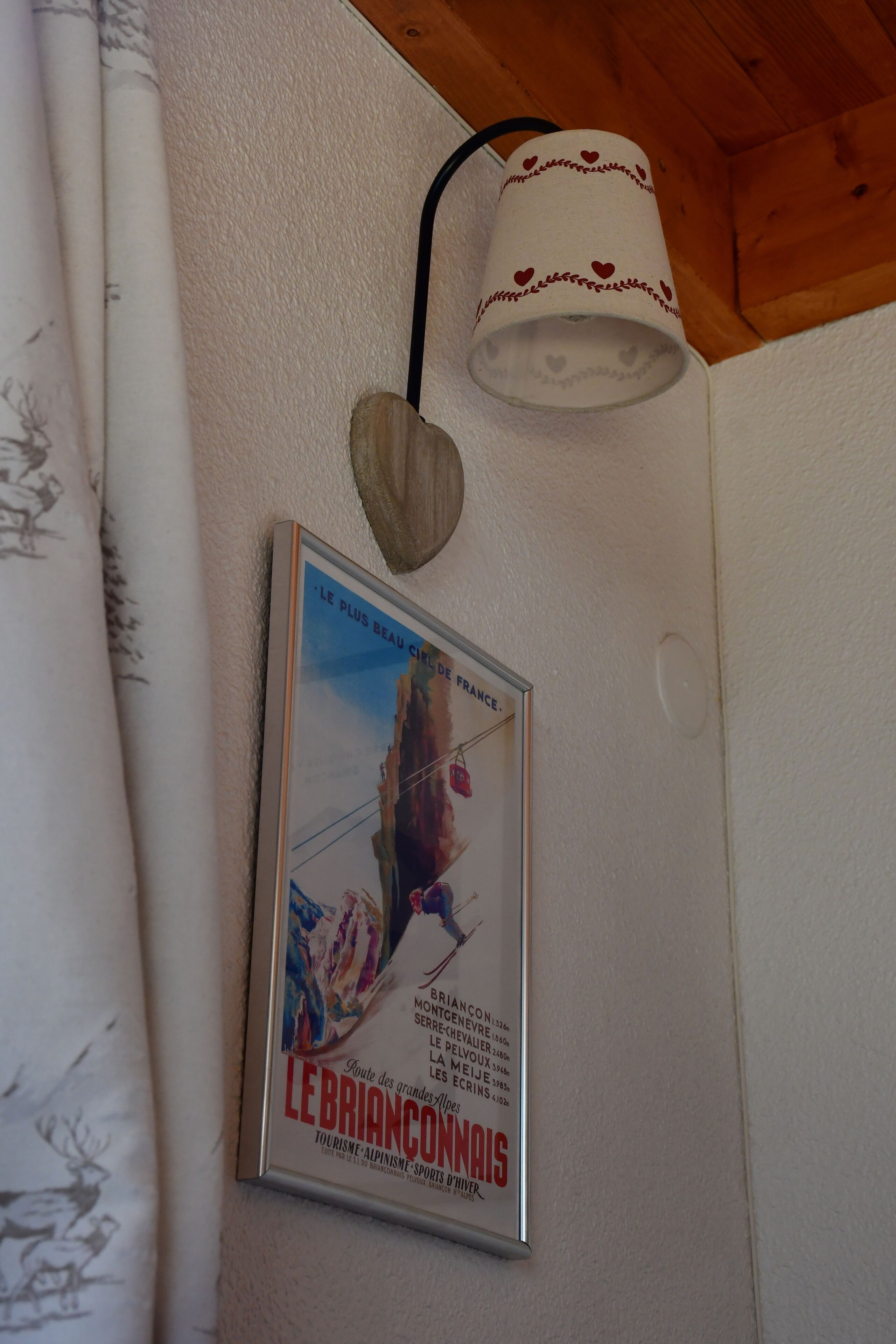 A framed poster of a mountain route, a heart-shaped light fixture, and a curtain with a pattern.