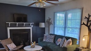A living room with a fireplace, a green sofa, a wooden floor, and a ceiling fan. - Enjoyable 2-bedroom cottage in Afton Virginia.
1.5 miles from the best winery! (Afton)