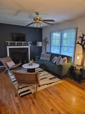 A living room with a fireplace, a green sofa, a wooden floor, and a ceiling fan. - Enjoyable 2-bedroom cottage in Afton Virginia.
1.5 miles from the best winery! (Afton)