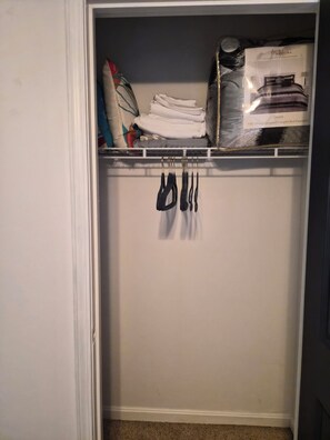 A closet with folded clothes, a bed, and hanging items.