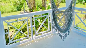 Una hamaca colgada de una baranda blanca, con vistas a un jardín exuberante de palmeras y al mar.