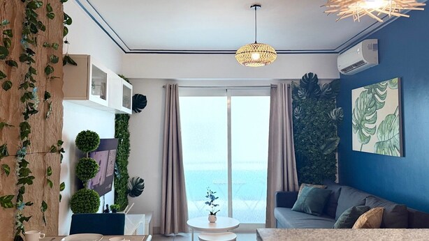 Ett modernt vardagsrum med en soffa, ett matbord och utsikt över havet genom stora fönster.