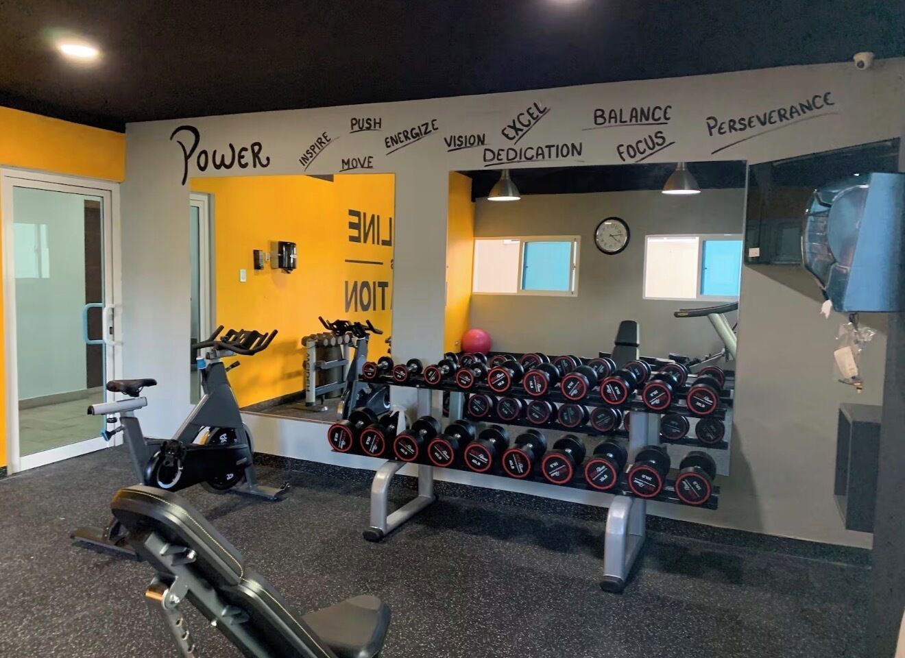 Ett gym med träningsutrustning, en vägg med motiverande ord och en spegel.