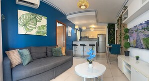 Una sala de estar moderna con un sofá, una mesa de centro y una zona de cocina con refrigerador y taburetes de bar.