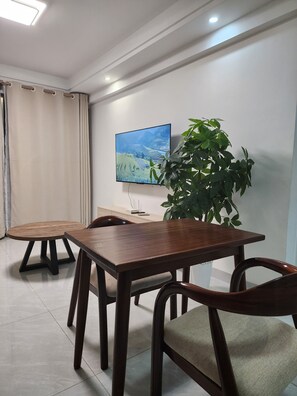 Ein moderner Essbereich mit Holztisch und Stühlen, einem großen Flachbildfernseher an der Wand und einem Blumentopf.