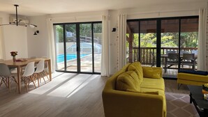 A modern living room with a yellow sofa, a dining area with a table and chairs, and a view of a swimming pool through large sliding doors. - Spacious Landes villa with swimming pool, in the heart of the pines (Soorts-Hossegor)