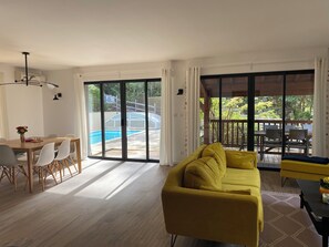 A modern living room with a yellow sofa, a dining area with a table and chairs, and a view of a swimming pool through large sliding doors. - Spacious Landes villa with swimming pool, in the heart of the pines (Soorts-Hossegor)