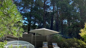 A swimming pool with a blue inflatable ring, surrounded by trees and a covered seating area with chairs and a table. - Spacious Landes villa with swimming pool, in the heart of the pines (Soorts-Hossegor)