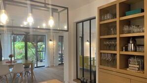 A dining area with a table set for two, a wine glass, and a cabinet with wine glasses and a coffee machine. - Spacious Landes villa with swimming pool, in the heart of the pines (Soorts-Hossegor)