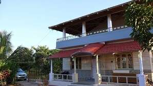 A two-story building with a balcony, a covered porch, and a car parked in front. - Anava Farms (Shrirangapattana)