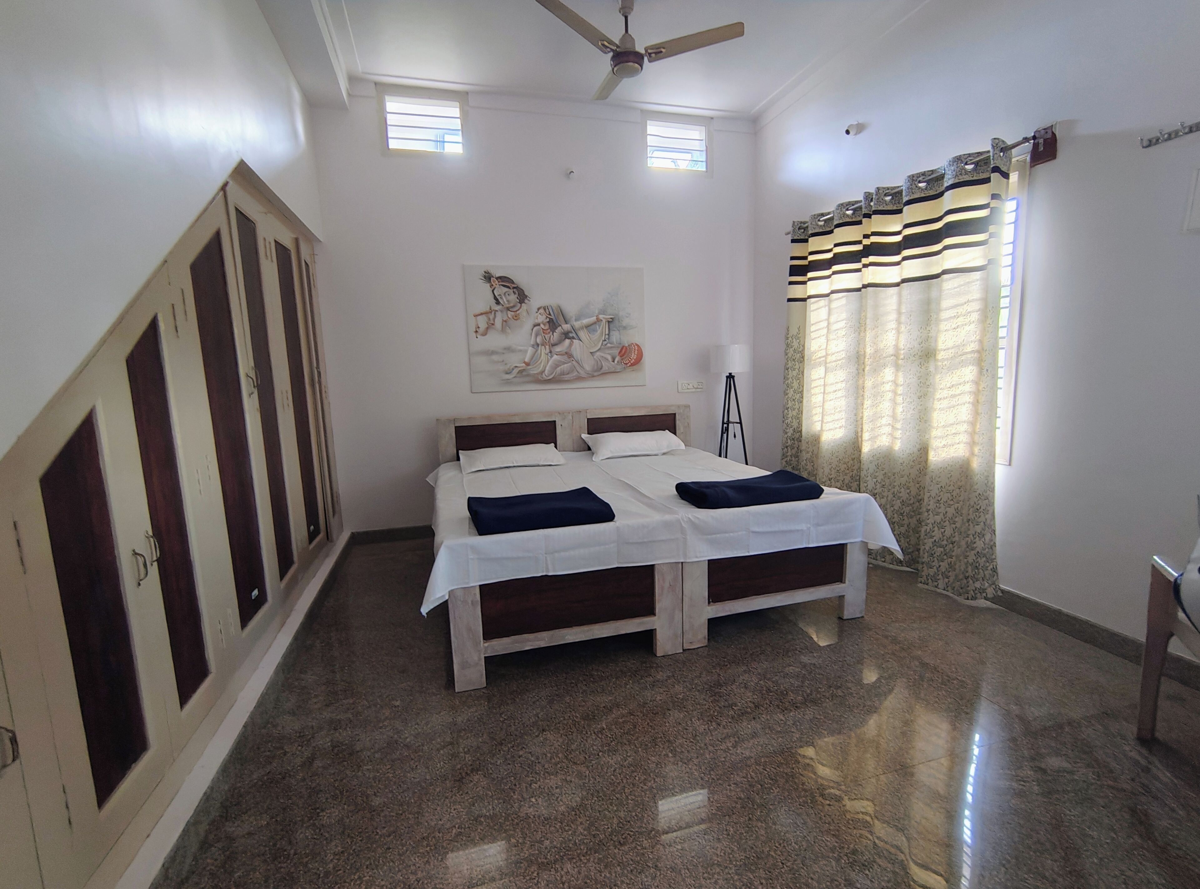 Un dormitorio con cama, armario, ventilador de techo, obras de arte y una ventana con cortinas.