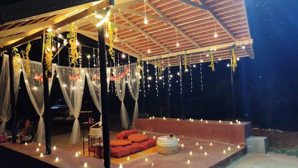 An outdoor covered area with a stage, seating, and string lights. - Anava Farms (Shrirangapattana)