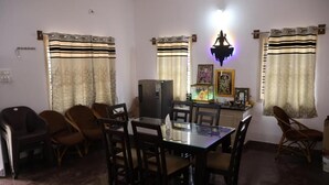 A dining area with a glass table, chairs, a refrigerator, and curtains. - Anava Farms (Shrirangapattana)