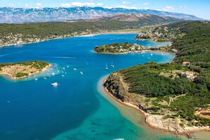 An aerial view of a coastal area with clear blue waters, boats, and a mountainous backdrop. - Seafront Studio on the Island of Rab (Rab)