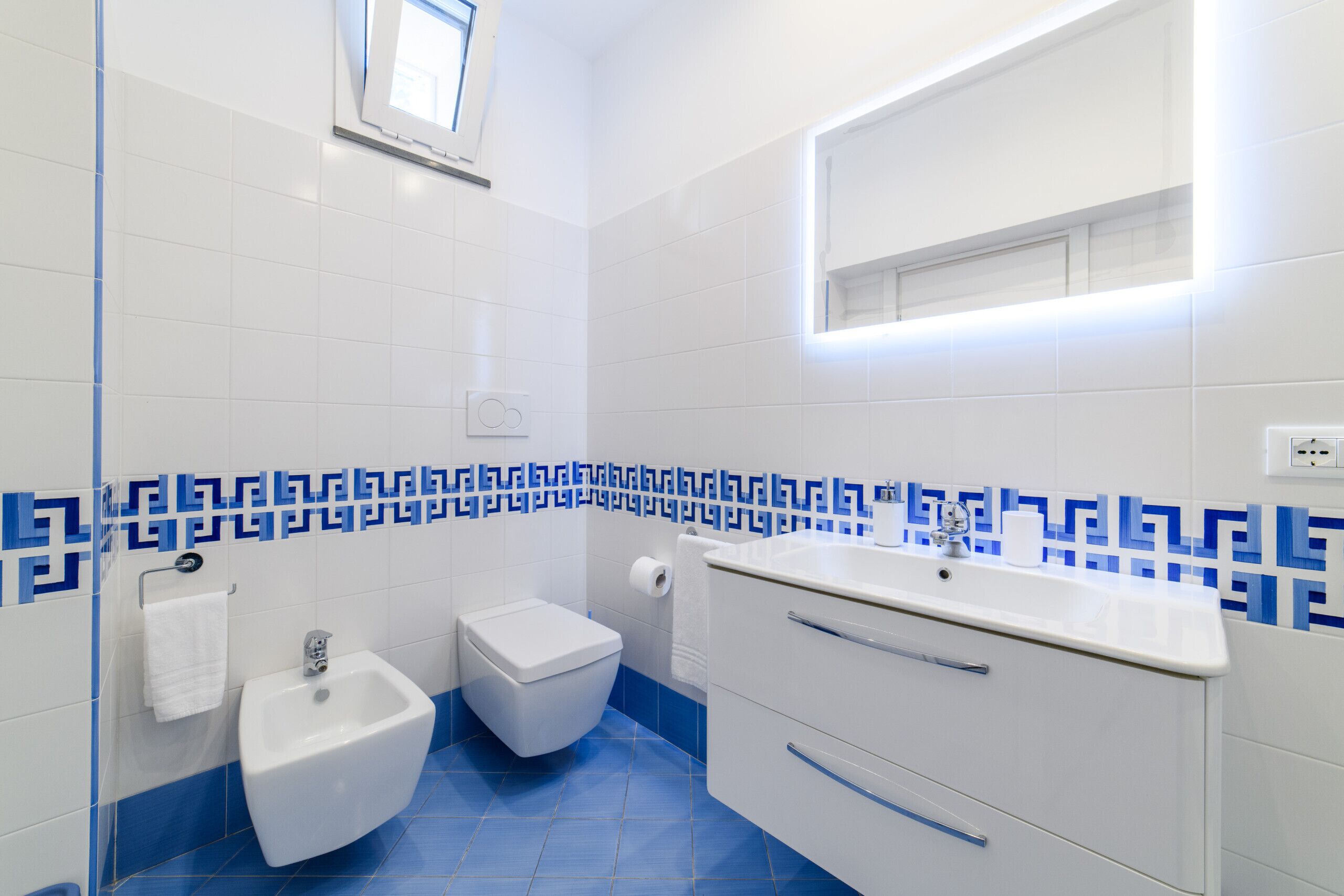 Een badkamer met een toilet, wastafel, spiegel en een bidet.