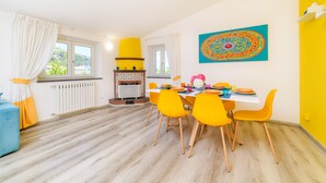 Un comedor con una mesa dispuesta para cuatro personas, sillas amarillas, un sofá azul y un cuadro decorativo grande en la pared.