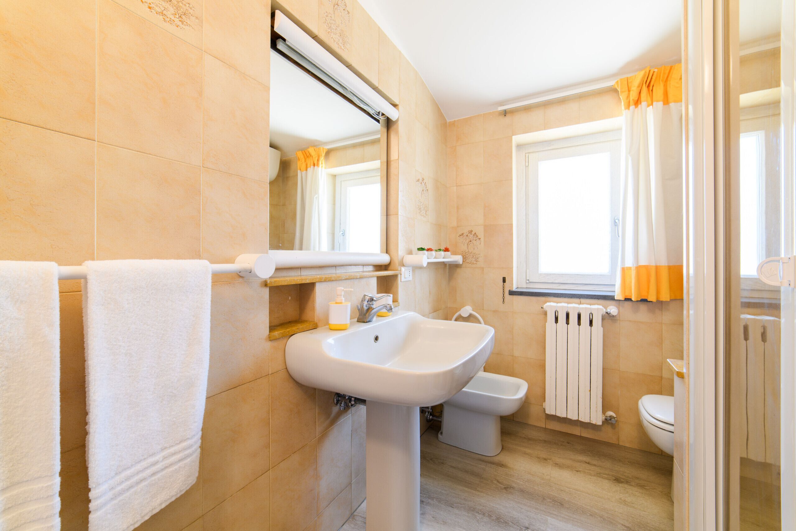 Un baño con lavamanos, inodoro y ventana con cortinas.