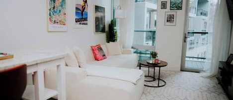 A modern living room with a white sofa, a small round table, and a balcony with a view.