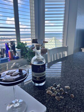 Eine Flasche ZARITA Espresso Martini auf einer Küchenarbeitsplatte, mit einem Glas des Getränks, einem weißen Teller und Muscheln.
