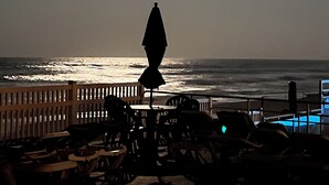 Une vue sur la plage, avec un océan baigné de soleil, une clôture en bois et une table entourée de chaises.