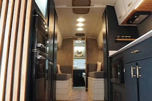 Un intérieur de camping-car compact comprenant un coin cuisine, un espace salon et une petite fenêtre.