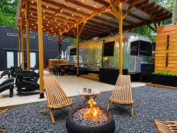 Un espace extérieur aménagé avec des fauteuils confortables, un foyer et une terrasse couverte illuminée de guirlandes lumineuses.