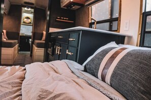 A bed with a striped pillow and a beige blanket, a black dresser with gold handles, and a window with a view.
