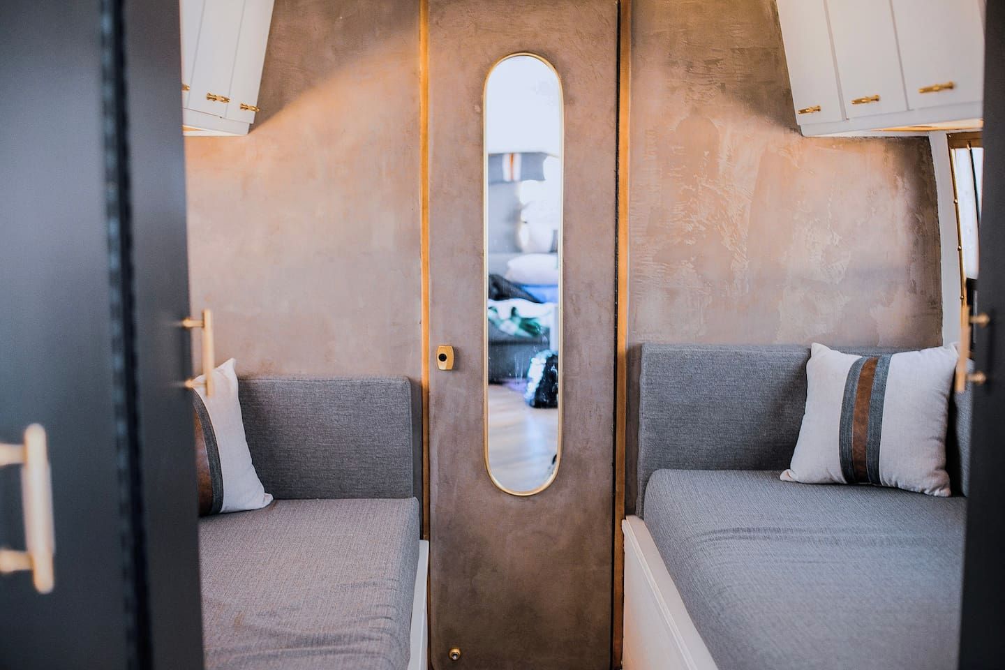 Ein kompaktes Wohnmobil-Interieur mit zwei Schlafbereichen, jeweils mit einem Bett und einem Kissen, sowie einer zentralen Tür mit Spiegel.