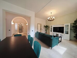 A modern living room with a dark wooden dining table, teal chairs, a green sofa, a TV, and a white cabinet. - Casa Albania Rome (Roma)