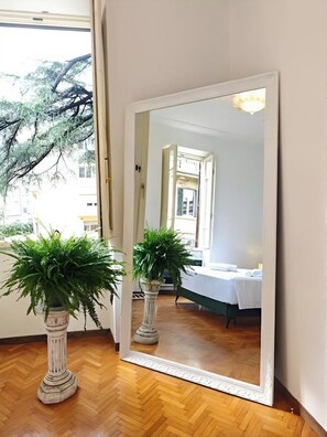 A room with a large mirror reflecting a bed and a window with a view of trees. There are two potted plants in front of the mirror. - Casa Albania Rome (Roma)