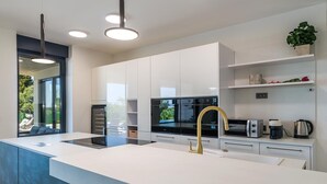 Een moderne keuken met een centraal eiland, geïntegreerde apparatuur en uitzicht door een groot raam.